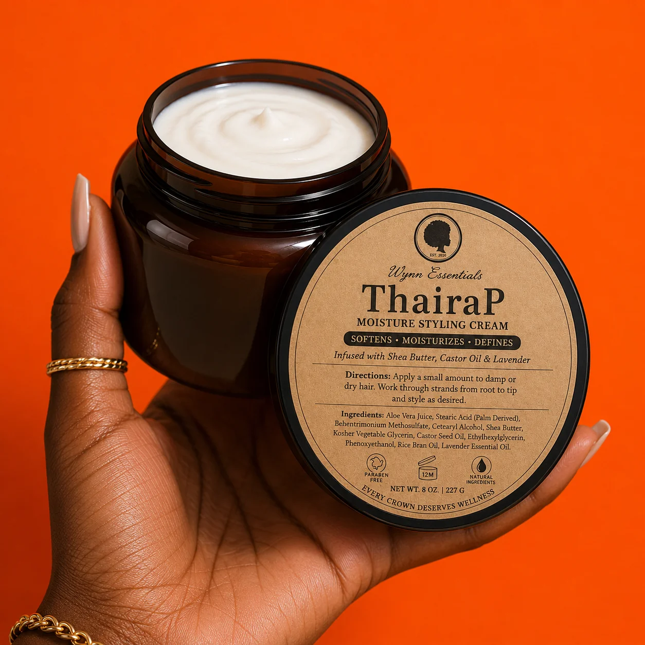 Open ThairaP Moisture Styling Cream jar held against a bright orange background